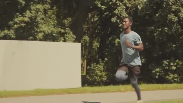 在阳光明媚的日子 追踪在公园人行道上跑步的年轻的非裔美国运动员的慢动作 — 图库视频影像