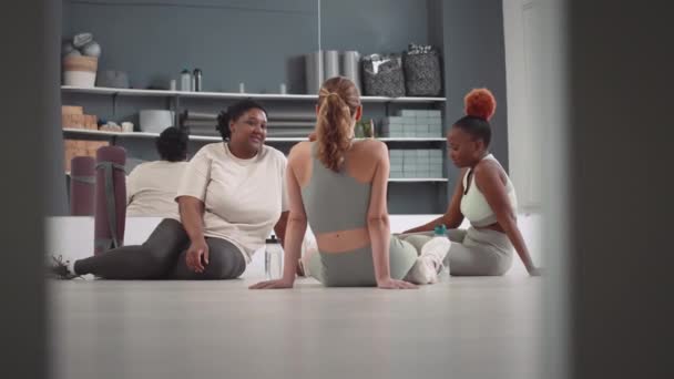 Trzy Młode Zróżnicowane Kobiety Rozmawiające Podczas Odpoczynku Podłodze Studiu Fitness — Wideo stockowe