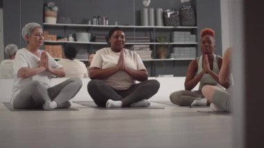 Dört farklı kadın Lotus 'ta oturmuş parlak modern yoga stüdyosunda birlikte meditasyon yapıyorlar.