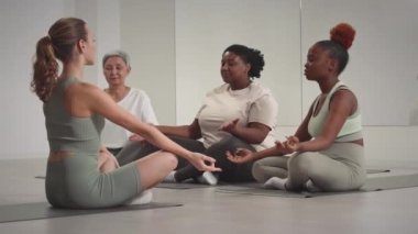 Çeşitli kadınlar ve kadın yoga hocaları minimalist stüdyoda oturmuş meditasyon yapıyorlar.
