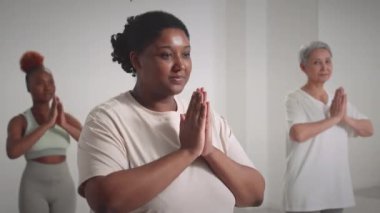 Minimalist yoga stüdyosunda dua eden ellerle kameraya bakan üç farklı nesil kadının belini kaldırın.