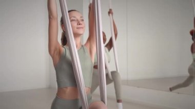 Geniş, parlak stüdyoda hava yogası yaparken ipek hamak tutan iki genç kadın.