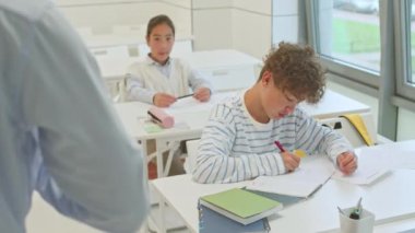 Sınıfta beyaz masalarda oturan iki çoklu ırkçı öğrenciye ders veren tanınmamış erkek öğretmenin omzunun üstünden not alıp, onları dinliyorlardı.