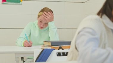 Beyaz sınıftaki beyaz masada oturan ve test yapan konsantre beyaz öğrencinin beline kadar.