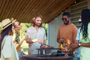 Yazın barbekü partisinde çeşitli arkadaşlarla dışarıda et ızgara yapan sakallı genç adamın portresi.