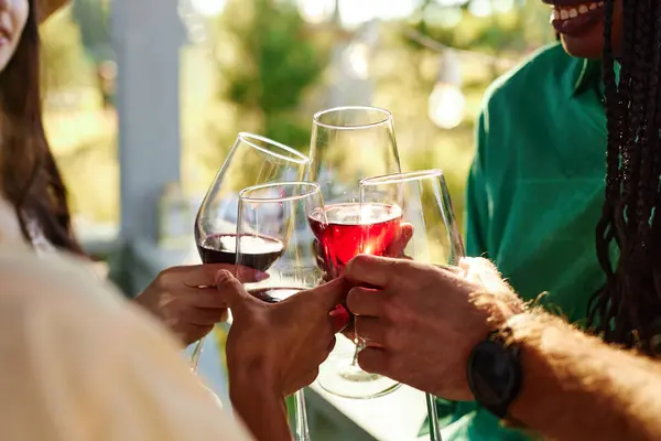 Close up of friends toasting with wine glasses in celebration during outdoor party in Summer