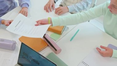 Ders sırasında masada çember halinde otururken matematik çalışma kağıtlarını öğretmene veren bir grup öğrencinin üst görünümü