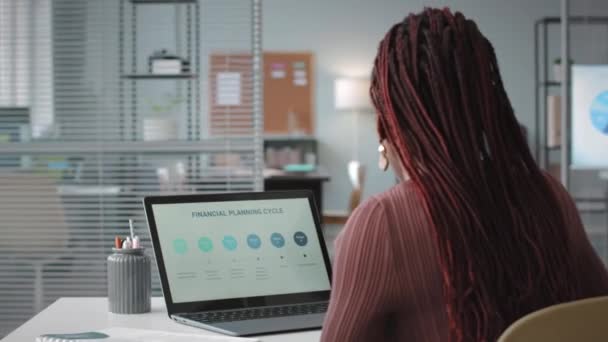 若いアフリカ系アメリカ人女性が ノートパソコンで財務計画サイクルを分析し オフィスで働いている間に書類作成をしています — ストック動画