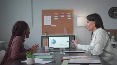 İki başarılı iş kadını ofiste çalışırken dizüstü bilgisayarda finansal slayt sunumunu tartışıyor.