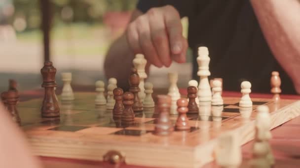 外でチェスをする2人の認識できない大人の男性 フォーカスされたフォアグラウンドの木製チェスボードのクローズアップ — ストック動画