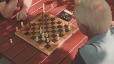 Dışarıda satranç oynayan iki konsantre yaşlı adam hamle yaptıktan sonra satranç saatinin düğmesine basıyor.