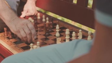 Güneşli bir günde, bankta satranç oynayan tanınmayan iki yetişkinin yakınına.