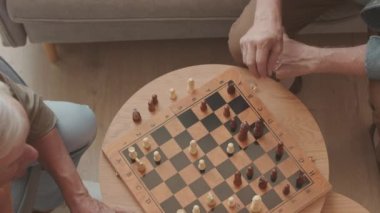 İki gri saçlı yetişkin adamın kapalı masa üzerinde satranç oynamalarının üst görüntüsü.