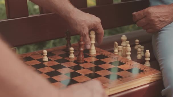 公園の木のベンチに座っている男性の友人とチェスをしながらチェックメイトを作る認識できない男のゆっくりとした動き — ストック動画