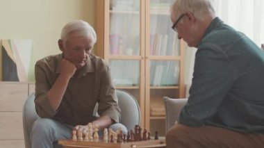 Parlak, rahat bir dairede satranç oynayan iki beyaz adamın orta boy fotoğrafı.
