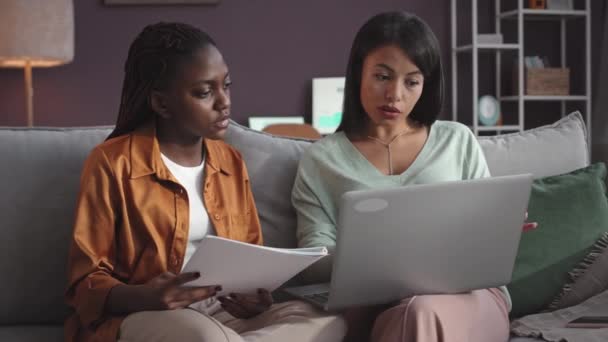 現代のホームオフィスでソファーで一緒に作業しながらビジネスプロジェクトのアイデアを議論する2人の若い多民族女性の同僚のミディアムショット — ストック動画
