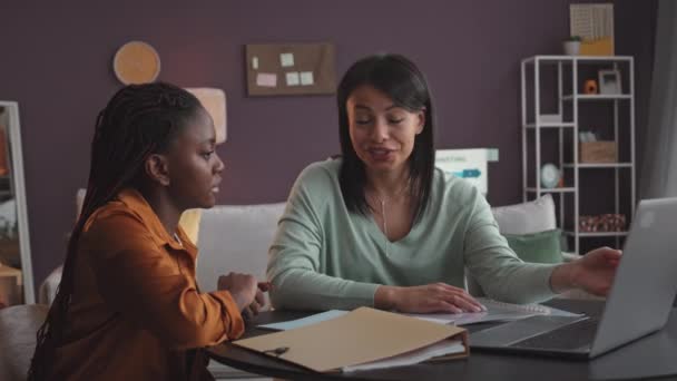 2人の若い多民族女性が 自宅オフィスでビジネスプロジェクトで一緒に仕事をしながら ノートパソコンで仕事を話し合うのを待っています — ストック動画