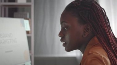 Genç Afrikalı Amerikalı bir kadının evde bilgisayardan marka pazarlama okurken kendi başına şarkı söylemesi.