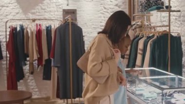 Modern tasarımcı giyim mağazasında alışveriş yaparken şık kıyafetlere ve aksesuarlara bakan iki genç kadının orta boy fotoğrafı.