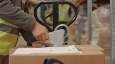 Tanınamayan bir depo çalışanının karton kutuları paketlemek ve fatura kağıdı imzalamak için yapışkan bant kullanmasının orta bölümü, nakliye ve sevkiyat için paket hazırlama