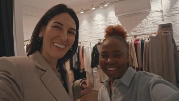 現代のデザイナーブティックで一緒に服を買いながら楽しんでいる2人の陽気な多民族女性の親友のハンドヘルドPov — ストック動画