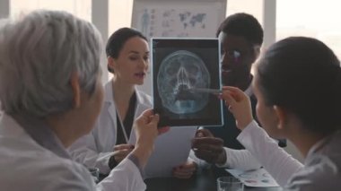 Beyaz laboratuvar önlüklü, çok ırklı profesyonel tıp ekibinin röntgen görüntülerini inceleyip teşhis koymaları ve çağdaş klinikte birlikte çalışmaları sayesinde.
