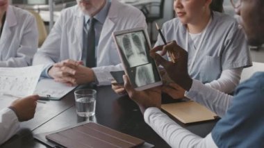 Çeşitli tıbbi ekipler dijital tablet üzerinde hastanın göğüs röntgenini analiz ediyor, modern klinikteki masada konferans veriyorlar.