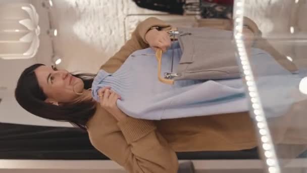 우아한 캐시미어 스웨터와 옷걸이에 스커트와 여자의 부티크에서 거울에서 자신을 — 비디오