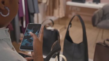 Siyahi bir kadının şık siyah ayakkabılı akıllı telefonuyla özel tasarım butikte alışveriş yaparken videosunu çekmesi.