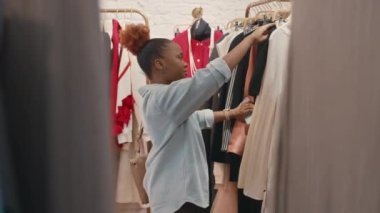 Genç, şık bir siyahi kadının lüks tasarımcı galerisinden şık kıyafetler seçtiği orta boy bir fotoğraf.