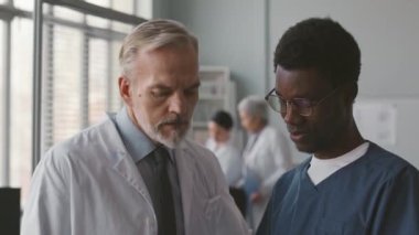 Genç siyahi erkek hemşire ve doktor konuştuktan sonra el sıkışıyor, çağdaş tıp kliniğinde birlikte çalışıyorlar.