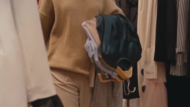 コンテンポラリーデザイナーブティックとクローズカーテンにフィッティングルームに入るハンガーに衣料品の山の認識できない女性のクローズドショット — ストック動画
