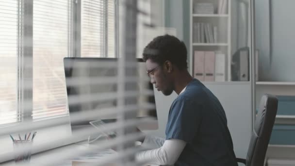 年轻的黑人男性医生坐到电脑前 在屏幕上分析病人的脊柱X光并进行诊断 — 图库视频影像