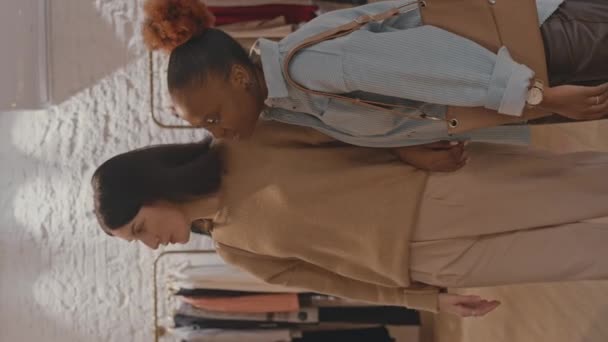 若い多民族の女性の友人の垂直ショット デザイナーのショールームで衣服を議論しながら一緒に服を買う — ストック動画