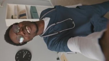 Çağdaş tıbbi klinikteki çalışmalarıyla ilgili video blogu kaydeden neşeli siyahi erkek hemşirenin el bilgisayarı.