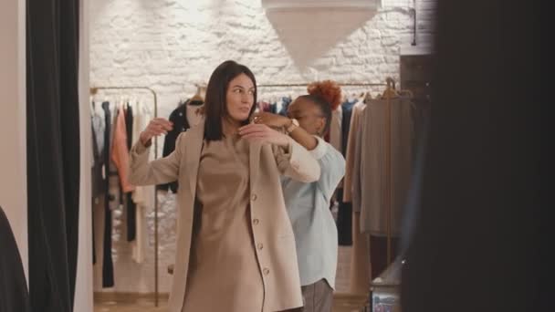 与女性朋友购物时 在豪华设计师陈列室试穿雅致骆驼外套的白人年轻女子中的一张照片 — 图库视频影像
