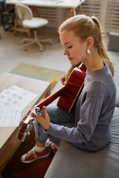 ソファーに座って音楽を作曲しながら 自宅でギターを弾く若い女性の垂直な肖像画 — ストック写真