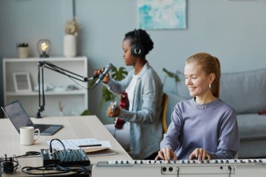 Sentezleyici çalan gülümseyen genç bir kadının portresi ve stüdyo arkadaşlarıyla müzik kaydı, kopyalama alanı.