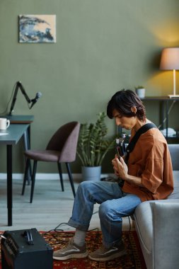 Ev müziği stüdyosunda elektro gitar çalan genç bir adamın dikey yan görünümü