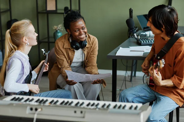 stock image Portrait of three young musicians writing songs together, focus on black woman smiling happily and holding music sheet