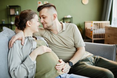 Genç mutlu çift oturma odasındaki kanepede dinleniyor ve birlikte hamileliğin tadını çıkarıyor.