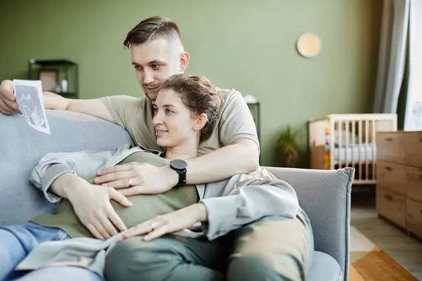 Young Couple Embracing Sofa Home Examining Ultrasound Scan Baby — Stock Photo, Image