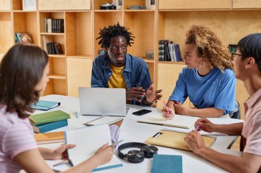 Kütüphane salonunda masada otururken proje üzerinde çalışan bir grup genç öğrenci.