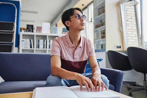 Low angle portrait of Asian young man reading book in tactile braille font in college library, copy space