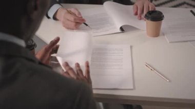 İki farklı takım elbiseli iş ortağının omuzlarının üzerinden. İş görüşmesinde başarılı bir anlaşma yaptıktan sonra sözleşmeyi okuyup el sıkışıyorlar.
