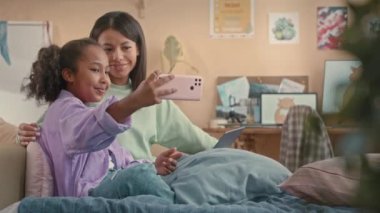 Mutlu 10 yaşındaki Afro-Amerikalı kız. Akıllı telefonuyla öz çekimini çekiyor. Annesiyle birlikte, sıcak çocukların yatak odasında, şeftali rengi duvarlı.