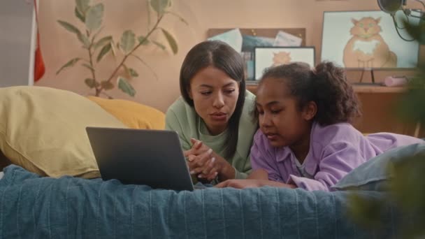 非洲裔美国人的母亲和十多岁的女儿一起使用笔记本电脑 边聊天边躺在舒适的带有桃墙的孩子卧室里 — 图库视频影像