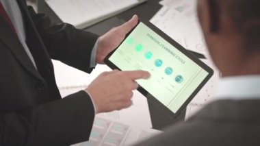 Tanımlanamayan iki farklı erkek iş ortağının dijital tablet üzerinden sunum istatistiklerini analiz etmesi, gündüz iş sırasında proje bütçesi planlaması