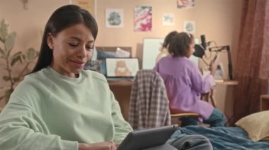Genç çift ırklı bir kadının dijital tablette sohbet ettiği belden yukarısı. Bu sırada kızı akıllı telefondan kayıyor ve arka planda bilgisayar masasının başında dans ediyor ve birlikte evde kalıyorlar.