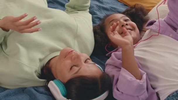 上記のショットから アフリカ系アメリカ人の母親と子供のベッドに横たわる19歳の娘が一緒にヘッドフォンでクールなポップミュージックを聞く — ストック動画